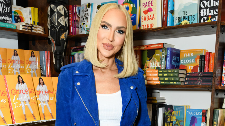 Christine Quinn in a bright blue blazer in front of bookshelves