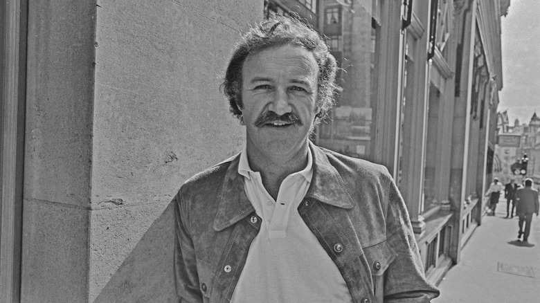 Young Gene Hackman smiles on a sidewalk