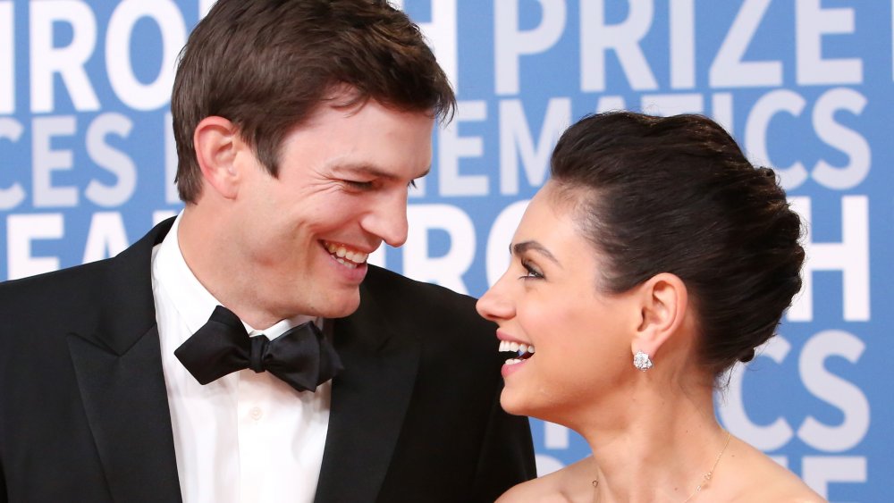 Ashton Kutcher, Mila Kunis smiling at each other on the red carpet