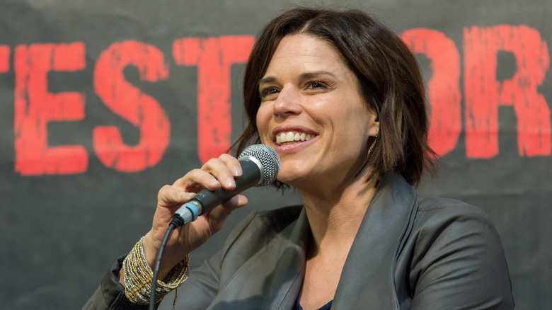 Neve Campbell smiling big and talking into a microphone