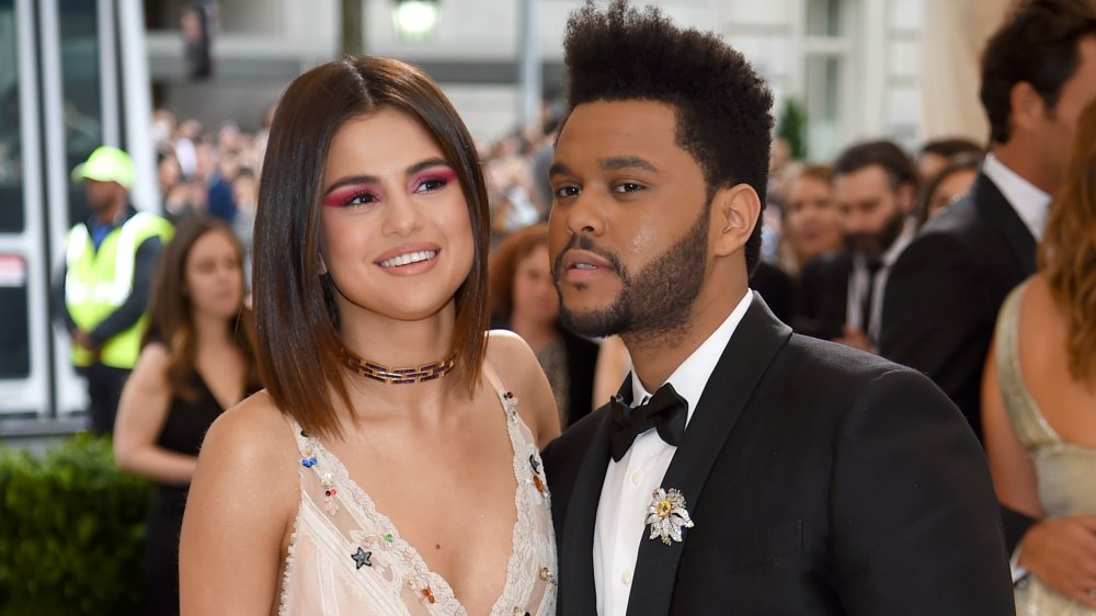 Selena Gomez in a white dress, The Weeknd in a black suit