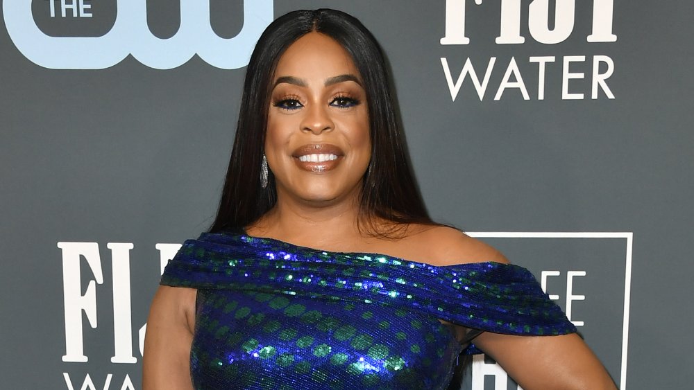 Niecy Nash in a blue-and-green dress, smiling with her hand on her hip