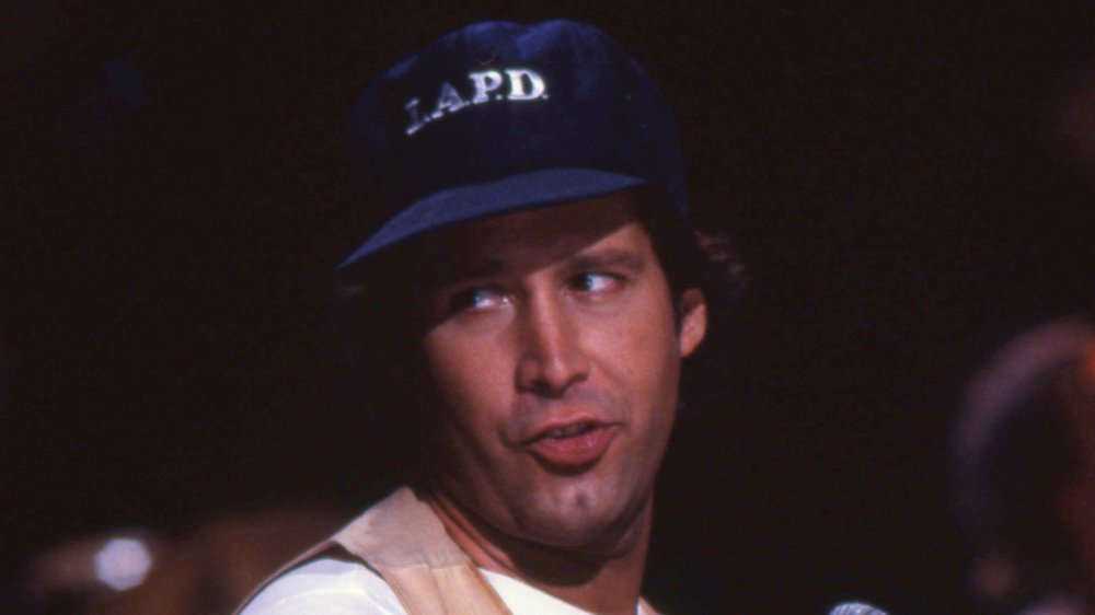 Chevy Chase speaking while looking off to the side and wearing a hat