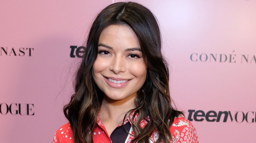 Miranda Cosgrove in a red, white, and black button up, smiling at a Teen Vogue event