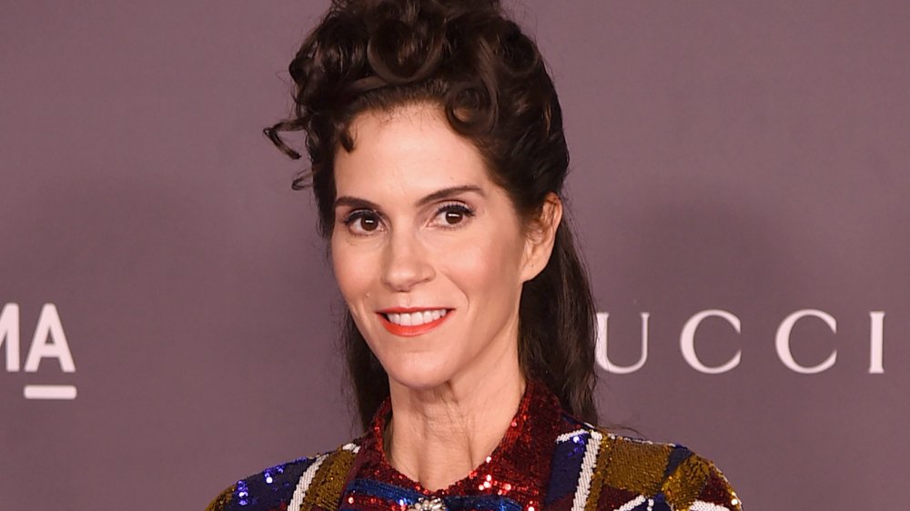 Jami Gertz in a red, blue, and gold sparkly dress, smiling and looking off to the side