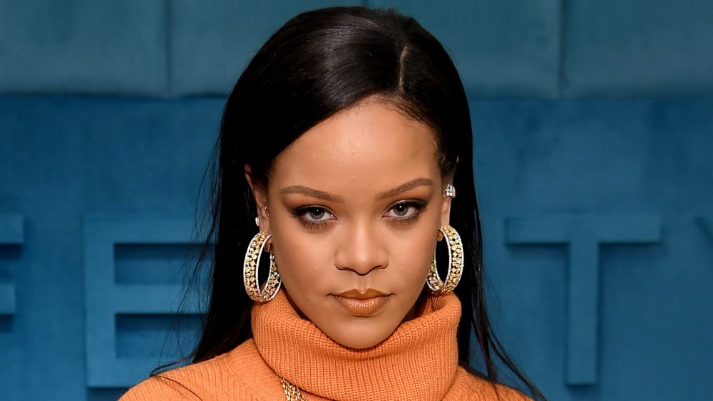 Rihanna in an orange turtle neck dress, posing with a serious expression