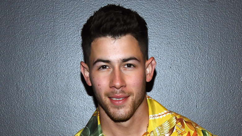 Nick Jonas smiles in front of black background