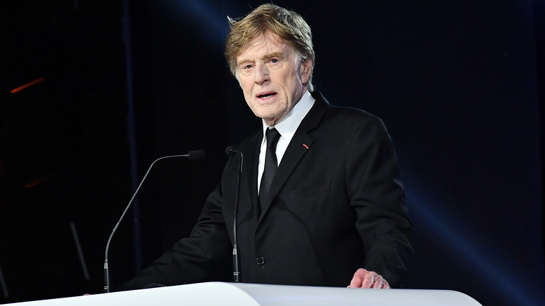 Robert Redford wearing a suit standing at a podium