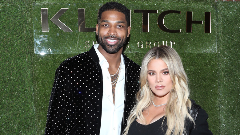 Khloé Kardashian posing with Tristan Thompson in front of a green background