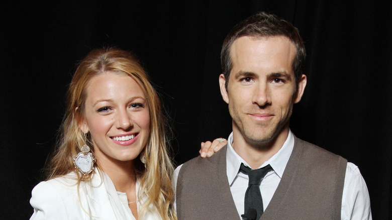 Blake Lively wearing a white jacket and large stone earrings and Ryan Reynolds wearing a grey vest, black tie, and white shirt