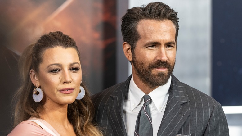 Blake Lively wearing a white gown and large hoop earrings and Ryan Reynolds wearing a grey pinstripe suit