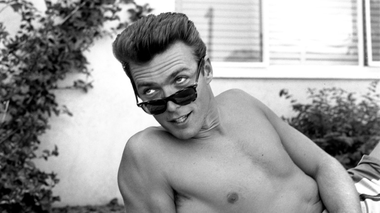 Clint Eastwood smiling through his sunglasses as he reclines, shirtless, in the 1950s