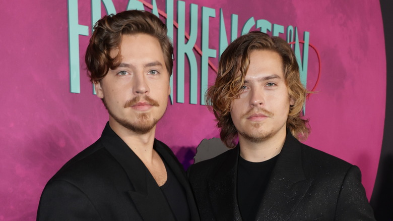 Cole and Dylan Sprouse wearing black jackets and black shirts while on a red carpet