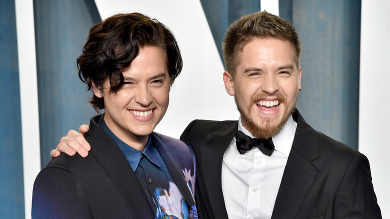 Cole Sprouse wearing a black and blue patterned suit and Dylan Sprouse wearing a traditional black suit and bowtie