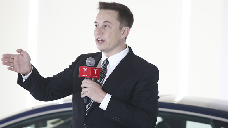 Elon Musk speaking by a Tesla 