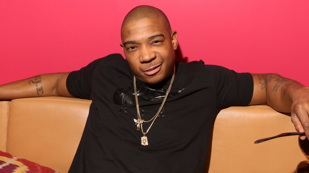 Ja Rule smirking in a black shirt, sitting on a brown leather couch