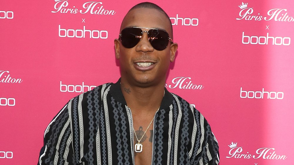 Ja Rule in a blue, black, and white patterned bomber jacket, wearing sunglasses and smiling