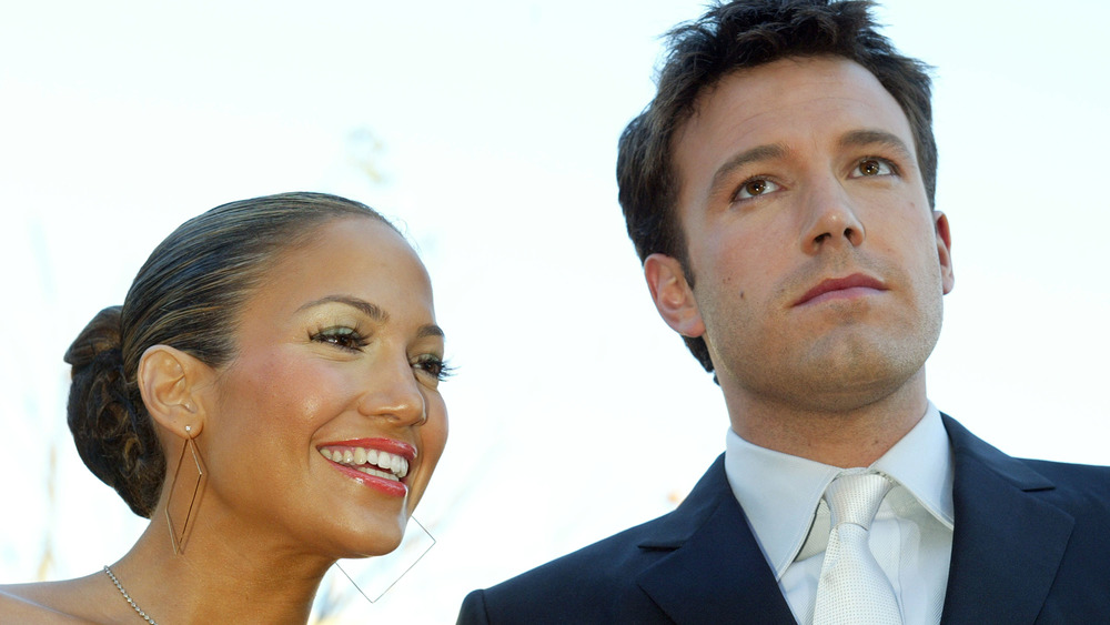 Jennifer Lopez smiling next to a somber-looking Ben Affleck