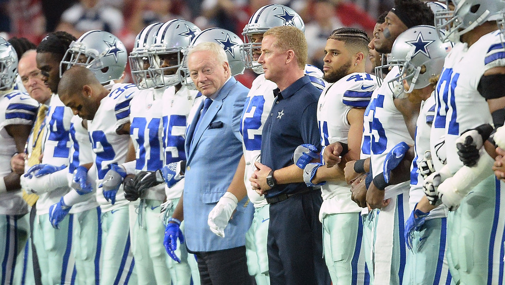 Jerry Jones standing on the field with the Dallas Cowboys locking arms during the national anthem