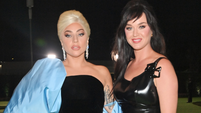 Lady Gaga wearing a black strapless gown with a blue sleeve and Katy Perry wearing a black spaghetti strap gown