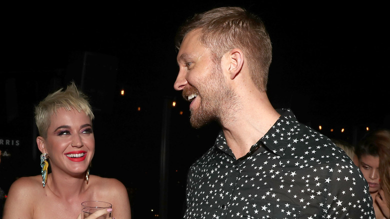 Katy Perry wearing large winged earrings laughing with Calvin Harris wearing a star-patterned collared shirt