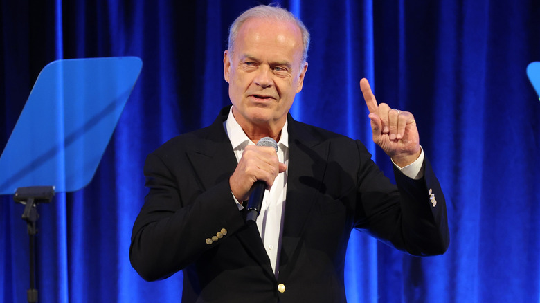 Kelsey Grammer speaking on stage, in front of blue curtains