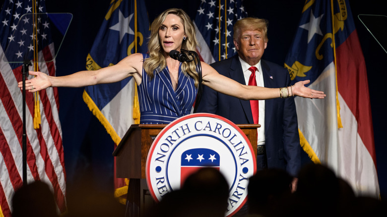 Lara Trump with arms outstretched at podium with Donald Trump behind