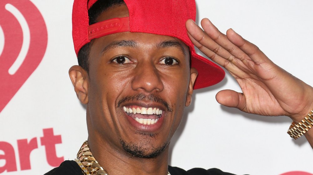 Nick Cannon saluting, wearing a red hat turned to the side 