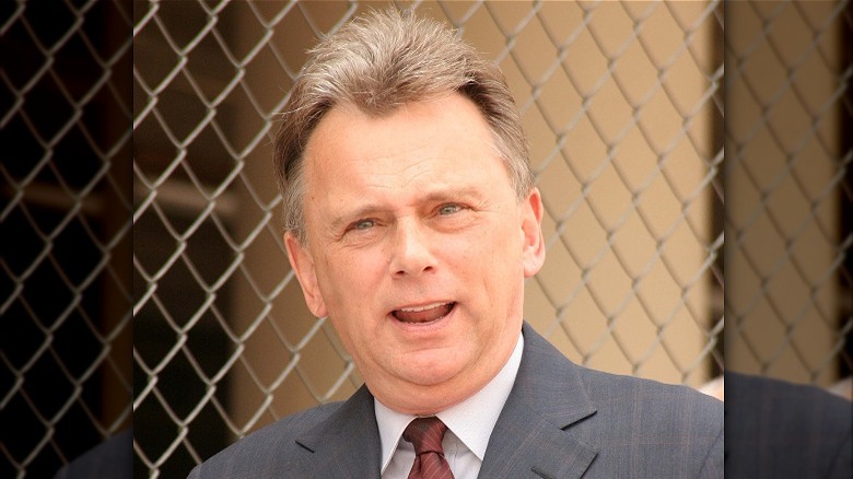 Pat Sajak speaking in front of a chain link fence