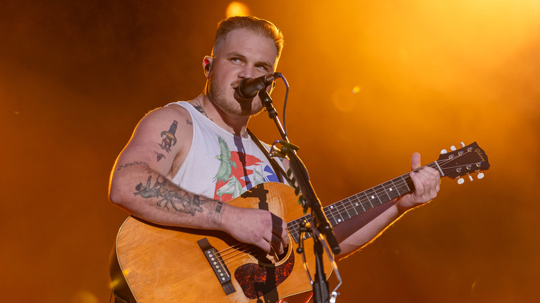 Zach Bryan singing and playing guitar on stage