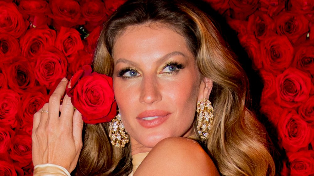 Gisele Bündchen holding a rose in front of a rose wall