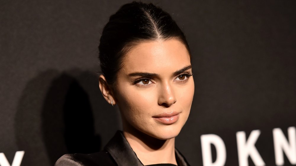 Kendall Jenner with her hair slicked back in front of black wall