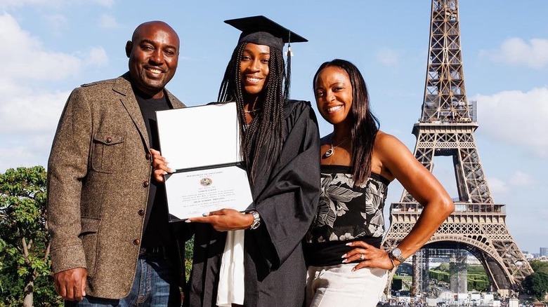 Coco Gauff wearing a cap and grown and standing with her parents posing with her diploma in front of Eiffel Tower