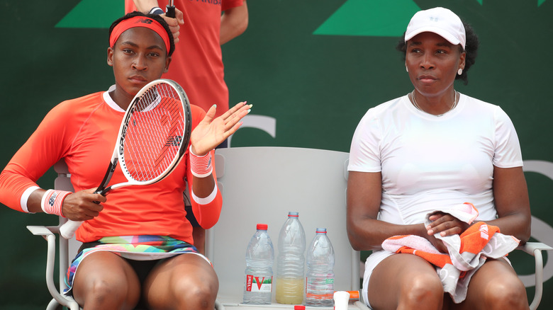 Coco Gauff sitting and holding racket beside Venus Williams