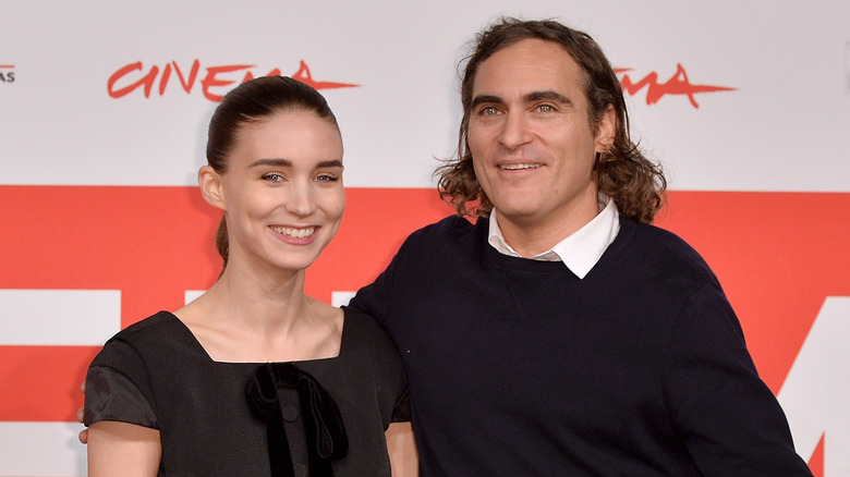 Rooney Mara wearing a black bowed dress and Joaquin Phoenix wearing a black sweater and white collared shirt