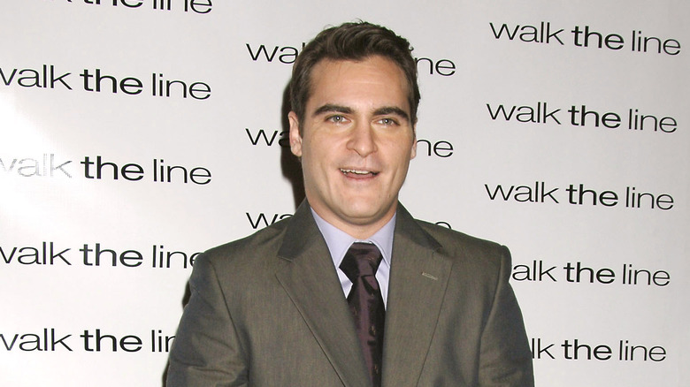 Joaquin Phoenix wearing a grey suit and purple tie on red carpet