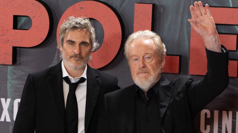 Joaquin Phoenix in a black suit and tie with Ridley Scott wearing a black suit at premiere