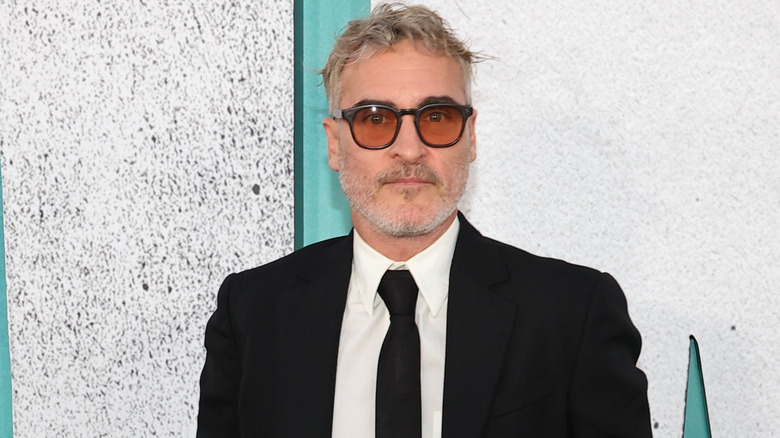 Joaquin Phoenix wearing tinted glasses and a black suit and tie on red carpet