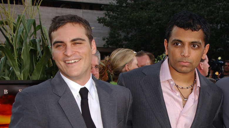 Joaquin Phoenix in a gray suit and black tie with M. Night Shyamalan wearing a gray suit and pink shirt