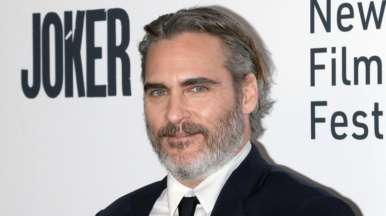 Joaquin Phoenix with slicked back greying hair wearing a black suit and tie at Joker premiere