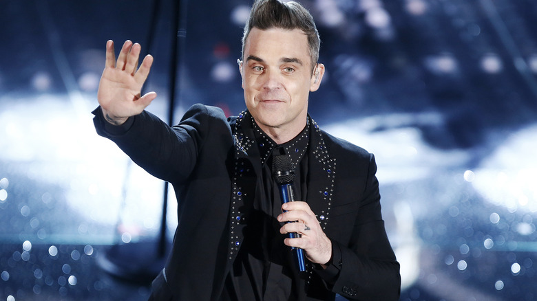 Robbie Williams on stage with hand in front of him