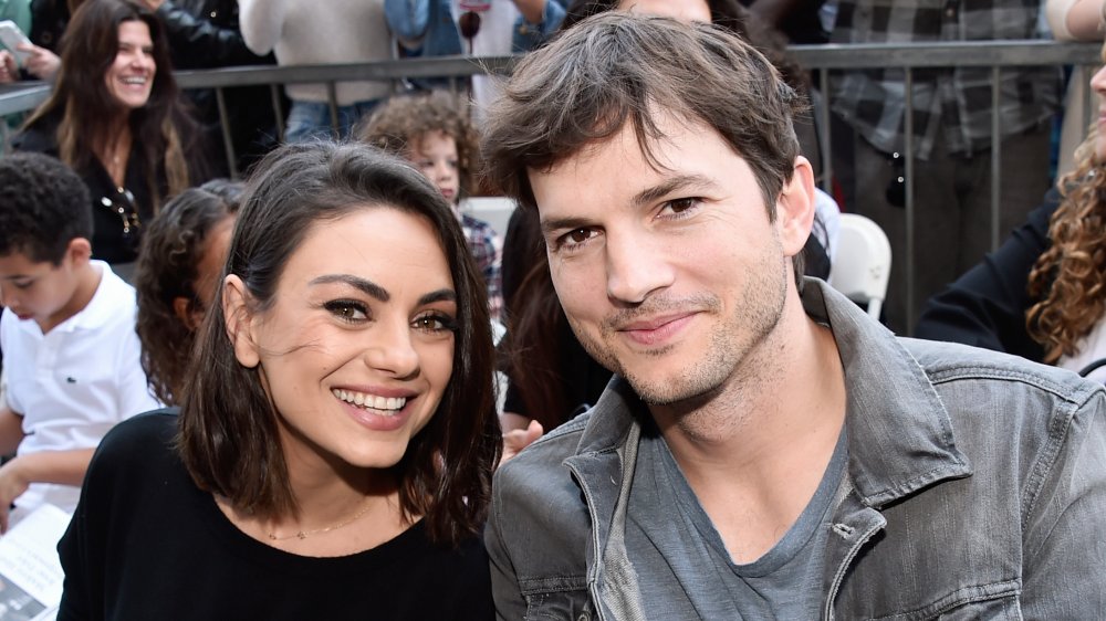 Mila Kunis and Ashton Kutcher, sitting and smiling at a 2018 Walk of Fame Star Ceremony
