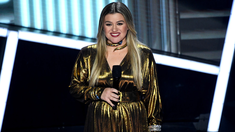 Kelly Clarkson smiling on stage with a microphone