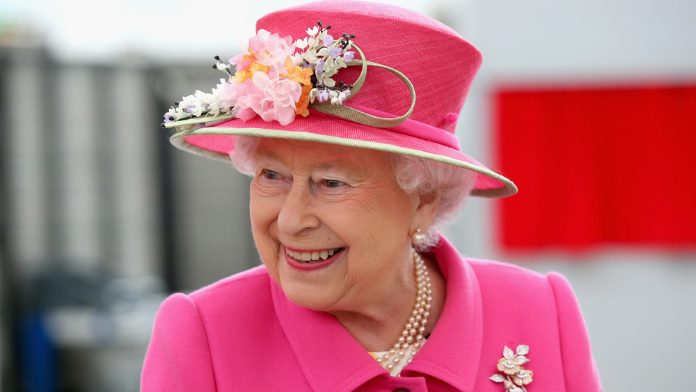 Queen Elizabeth II smiling at an event while wearing bright pink