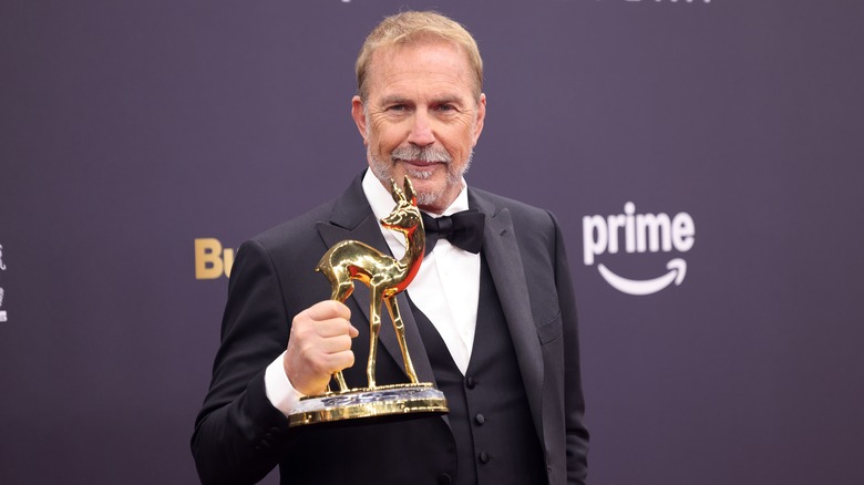 Kevin Costner holding a gold Bambi Award in a tuxedo