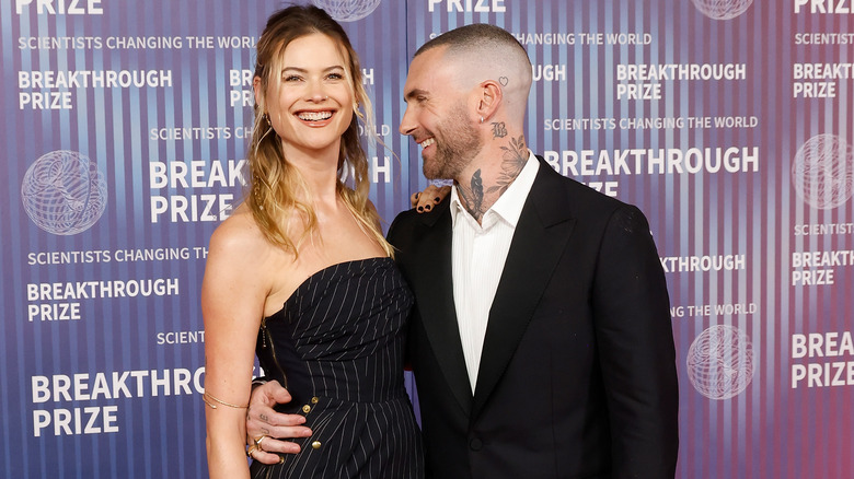 Behati Prinsloo and Adam Levine laughing together on the red carpet.