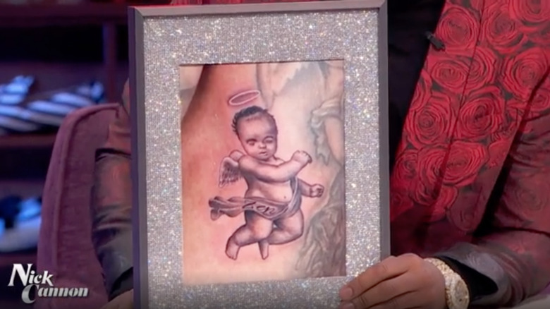 Nick Cannon holding up a photo of his tattoo