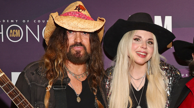 Billy Ray Cyrus and Firerose posing together on the red carpet.