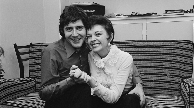 Judy Garland and Mickey Deans hold hands on the couch