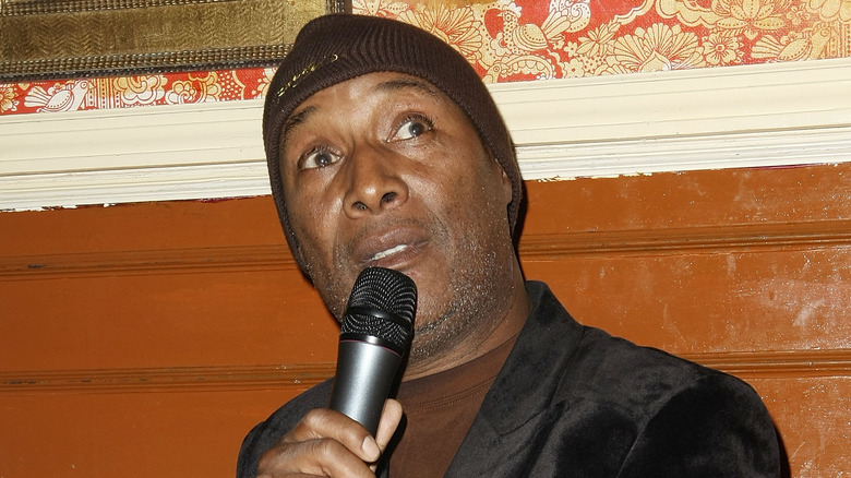 Paul Mooney looks up holding microphone